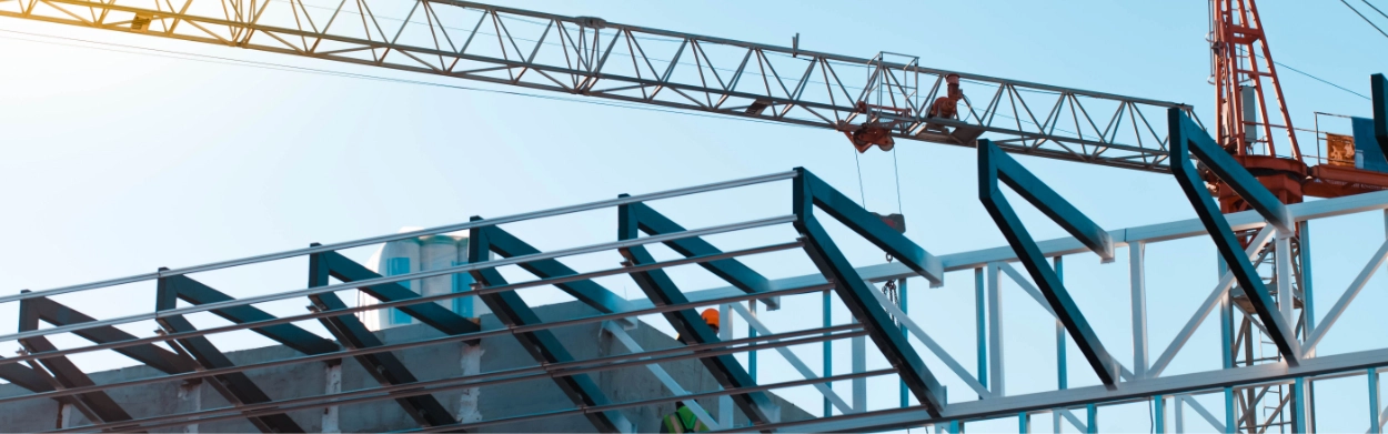 A construction crane operates above a steel framework structure under a clear sky, showcasing progress on a Metal Building Re-Roof project.
