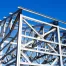 Steel framework of a pre-engineered metal building under construction rises against a clear blue sky.