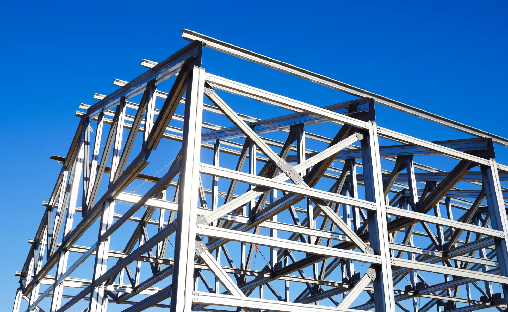 Steel framework of a pre-engineered metal building under construction rises against a clear blue sky.