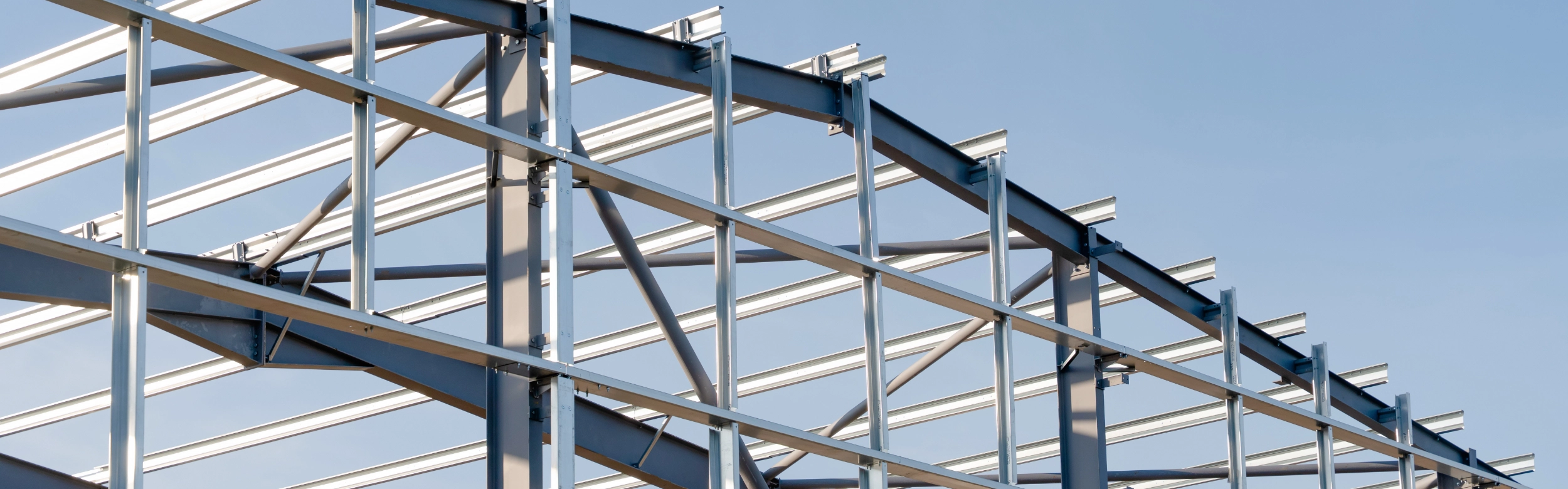 A partial view of a steel framework structure under construction against a clear blue sky, expertly crafted by a skilled metal building contractor.
