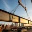 Construction site at sunset featuring crane lifting steel beam.